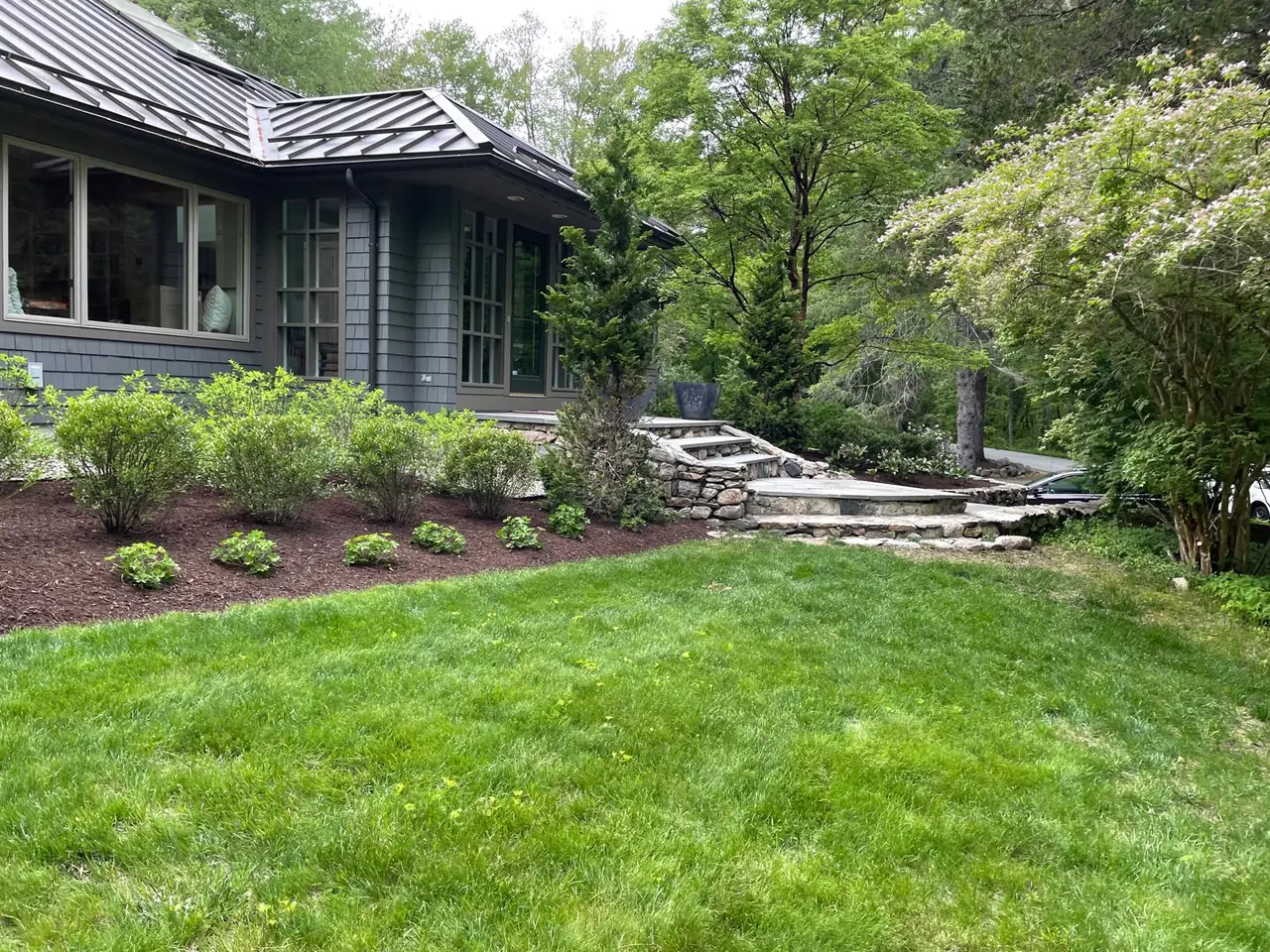 Dark gray home with lawn, layered planting, stone steps, and walls
